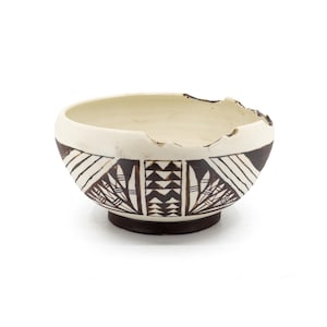 Può includere: Una ciotola in ceramica fatta a mano con interno color crema e base marrone scuro. La ciotola presenta un motivo geometrico in bianco e nero e un bordo leggermente scheggiato. Il design ricorda la ceramica dei nativi americani.