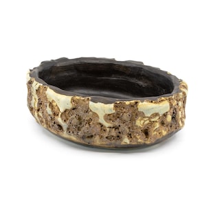 May include: An oval-shaped ceramic bowl with a textured, rough exterior. The rim and interior are dark brown, while the exterior features a mottled pattern of brown, beige, and light green. The bowl sits on a white background.