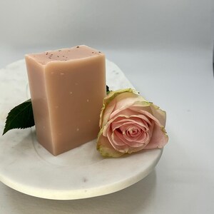 Może przedstawiać: Jasnor&oacute;żowe mydło w kostce z r&oacute;żą na białym marmurowym talerzu.