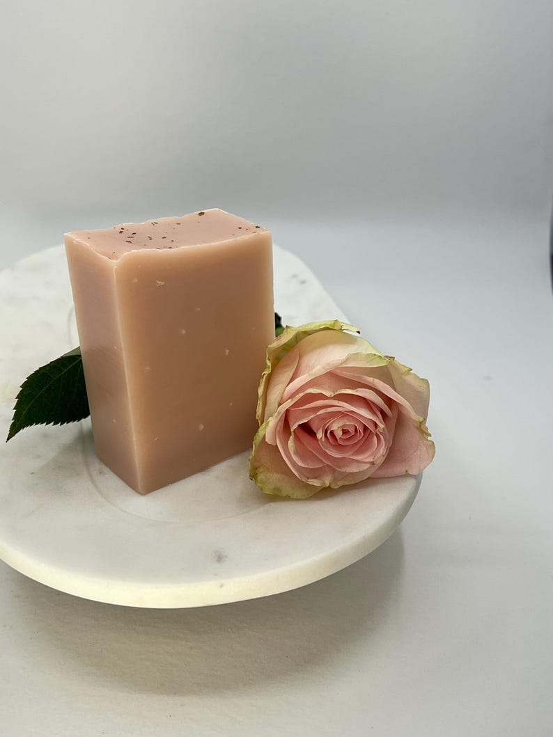 Może przedstawiać: Jasnor&oacute;żowe mydło w kostce z r&oacute;żą na białym marmurowym talerzu.