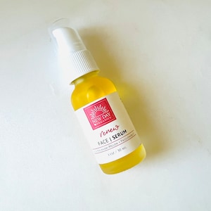 Puede incluir: Una botella de vidrio transparente de New Day Organics Renew Face Serum con una tapa de bomba blanca. El suero amarillo est&aacute; etiquetado con texto rojo y un logotipo de sol. La botella contiene 30 ml de suero.