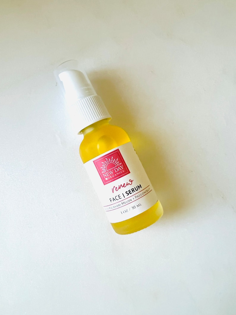 Puede incluir: Una botella de vidrio transparente de New Day Organics Renew Face Serum con una tapa de bomba blanca. El suero amarillo est&aacute; etiquetado con texto rojo y un logotipo de sol. La botella contiene 30 ml de suero.