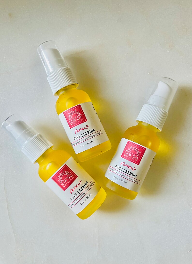 Puede incluir: Tres peque&ntilde;os frascos de suero amarillos con tapas de pulverizaci&oacute;n blancas est&aacute;n dispuestos sobre una superficie blanca. Cada frasco tiene una etiqueta con el texto "Renew FACE | SERUM" y "1 OZ / 30 ML". Las etiquetas tambi&eacute;n incluyen las palabras "NEW DAY ORGANICS".