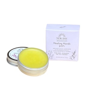May include: A small tin of yellow balm labeled "Healing Hands balm" by New Day Organics. The balm is infused with lavender and calendula oils, frankincense and myrrh. It is for dry, scraped or cut hands. The tin is 0.85 oz (24g).