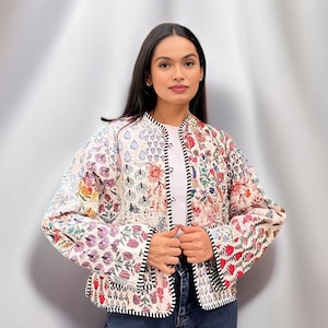 May include: A white quilted jacket with a floral patchwork design. The jacket has a mandarin collar, long sleeves, and a button closure. The jacket is trimmed with black piping.