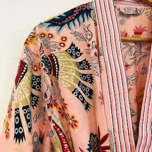 May include: A pink and white cotton robe with a floral print and pink and white striped trim. The robe has a long sleeve and a tie closure.