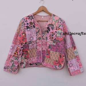 May include: A pink quilted jacket with a floral patchwork design. The jacket has a V-neck and long sleeves. The fabric is a mix of different prints and colors, including pink, red, and green. The jacket is trimmed with a white stitching.