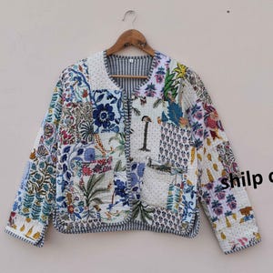 May include: A white quilted jacket with a patchwork design featuring floral and geometric patterns in shades of blue, green, and pink. The jacket has a button closure and a pocket on the left side. The text "shilp crafts" is visible on the right side of the jacket.