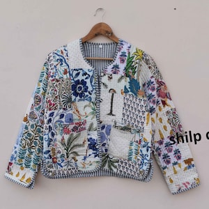 May include: A white quilted jacket with a patchwork design featuring floral and geometric patterns in shades of blue, green, and pink. The jacket has a button closure and a pocket on the left side. The text "shilp crafts" is visible on the right side of the jacket.