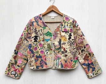 May include: A long-sleeved, quilted jacket featuring a patchwork design with various floral and botanical patterns in shades of pink, blue, green, and yellow on a cream background. The jacket has a V-neckline and a front button closure.