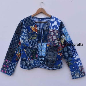 May include: A blue and white patchwork quilted jacket with floral and paisley patterns. The jacket has a V-neck and long sleeves.