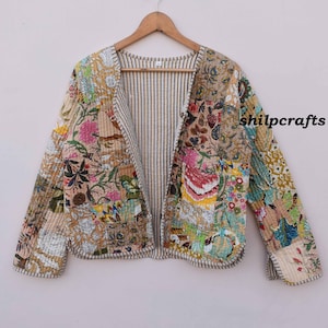 May include: A cream-colored quilted jacket with a floral print and a striped lining. The jacket has a V-neck and long sleeves. The text "shilpcrafts" is printed on the right side of the jacket.