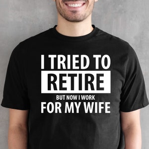 May include: Black t-shirt with white text that reads "I tried to retire but now I work for my wife."