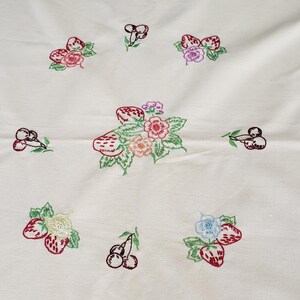 May include: Cream-colored fabric with embroidered designs of strawberries, cherries, and flowers. The embroidery features red, pink, purple, and green colors. The arrangement of the embroidered elements is scattered across the fabric.