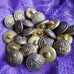 May include: A collection of round metal buttons featuring a raised design of a crown and crossed scepters. The buttons have a metallic gold and darkened bronze finish with a detailed border. Each button includes a shank on the back for attachment.