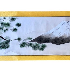 May include: A Japanese-style watercolor painting on a scroll. The artwork depicts a snow-capped mountain and a tree with green foliage. The painting is framed by a gold border.