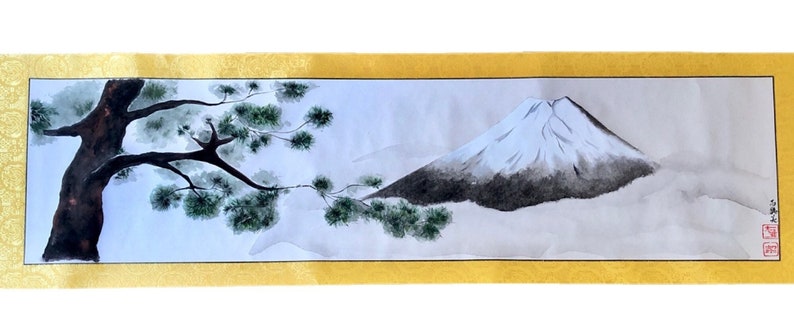 May include: A Japanese-style watercolor painting on a scroll. The artwork depicts a snow-capped mountain and a tree with green foliage. The painting is framed by a gold border.