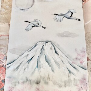 May include: A painting depicting Mount Fuji with two cranes soaring in the sky. The artwork includes a full moon, clouds, and cherry blossoms in white, grey, and pink. The painting has a tranquil, traditional Japanese style.