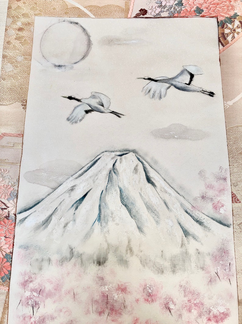 May include: A painting depicting Mount Fuji with two cranes soaring in the sky. The artwork includes a full moon, clouds, and cherry blossoms in white, grey, and pink. The painting has a tranquil, traditional Japanese style.