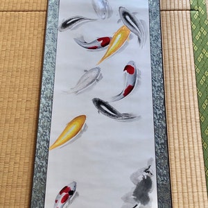 May include: A Japanese scroll painting featuring koi fish in shades of red, yellow, black, and white. The artwork is mounted on a dark blue fabric with a decorative border and wooden dowels.
