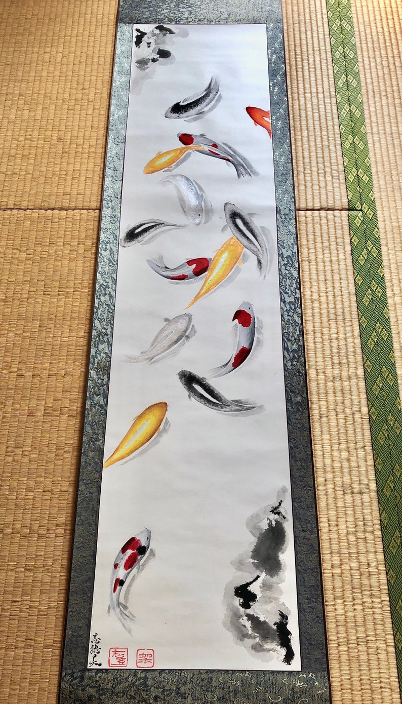 May include: A vertical scroll painting featuring koi fish in shades of black, white, red, and gold. The fish are depicted swimming in a flowing, abstract style. The artwork is framed with a decorative border and includes Japanese characters.