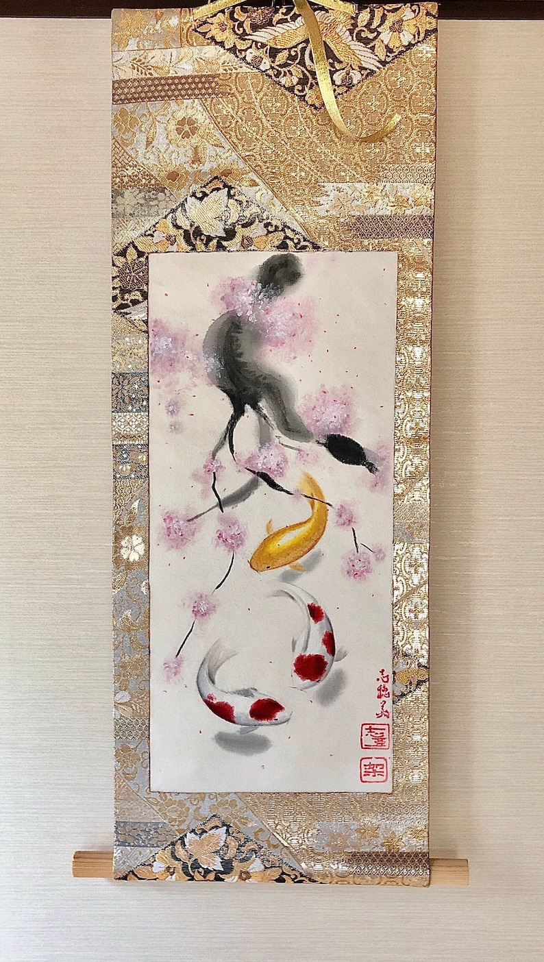 May include: Japanese scroll painting featuring a black bird perched on a cherry blossom branch, with two koi fish swimming below. The artwork is framed with gold and patterned fabric, and includes Japanese characters.