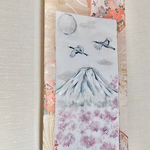 May include: Japanese scroll painting depicting Mount Fuji, cherry blossoms, and cranes. The artwork is set against a decorative fabric with floral and geometric patterns. The painting includes a full moon and clouds.