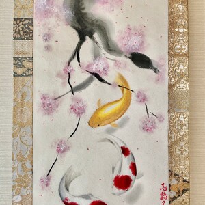 May include: Watercolor painting of two koi fish swimming beneath a cherry blossom branch. The fish are white with red markings and gold. The painting has a traditional Japanese style with decorative borders.