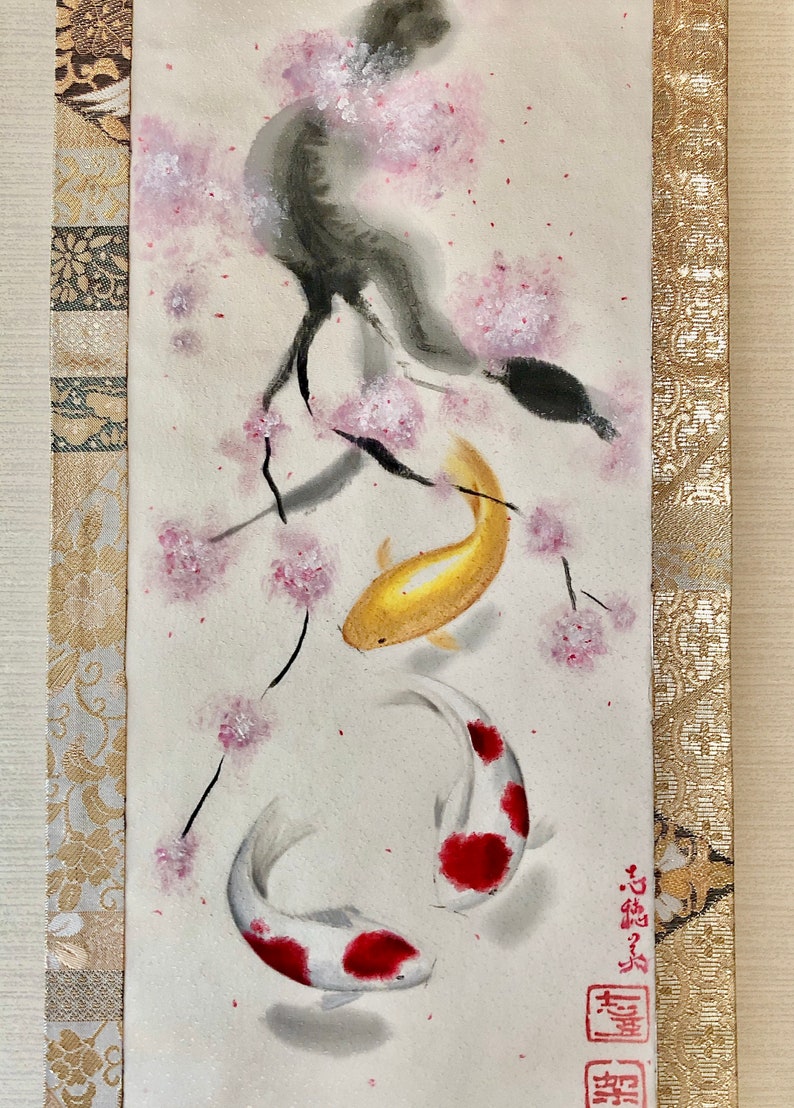 May include: Watercolor painting of two koi fish swimming beneath a cherry blossom branch. The fish are white with red markings and gold. The painting has a traditional Japanese style with decorative borders.