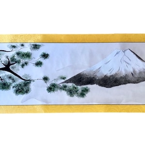 May include: A Japanese-style scroll painting featuring a mountain landscape. The artwork depicts a snow-capped mountain, a tree with green foliage, and a misty atmosphere. The scroll has a gold border and decorative end pieces.