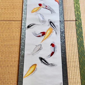 May include: A vertical scroll painting featuring koi fish in shades of black, white, red, and gold. The fish are depicted swimming in a minimalist style against a white background. The scroll has a dark border and a decorative top.