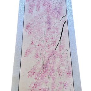 May include: A vertical Japanese scroll painting featuring a cherry blossom design. The artwork depicts delicate pink blossoms and branches against a light background. The scroll is framed with a silver border.