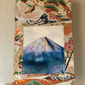 May include: A Japanese-style wall hanging featuring a painting of Mount Fuji with a snow-capped peak. The artwork is framed by ornate fabric panels with gold, orange, and cream colors, and traditional Japanese motifs.