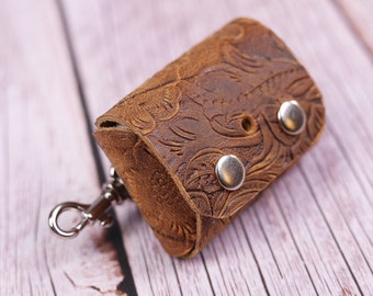 May include: A brown leather key chain with a floral embossed design and a silver metal clasp. The keychain has two silver metal snaps.