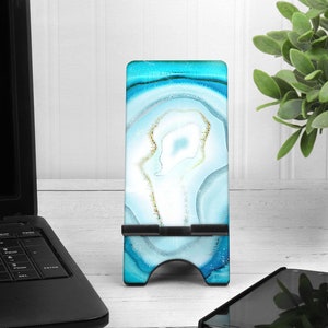 May include: A blue and white agate phone stand with a black metal base. The stand is on a white wooden surface.