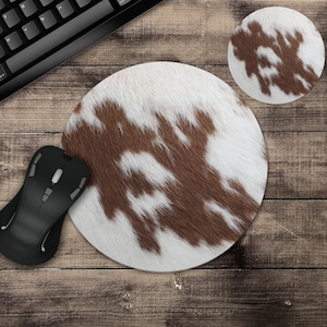 May include: A brown and white cowhide mouse pad with a round shape. The mouse pad is on a wooden surface.