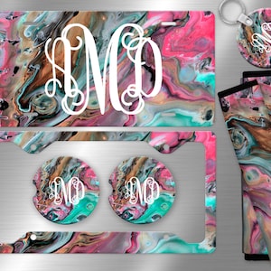 May include: A set of car accessories featuring a pink, teal, and brown abstract swirl pattern. The set includes a license plate frame, two car coasters, a key chain, and two seatbelt covers. The monogram "SMO" is featured on each item.