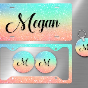 May include: A set of personalised car accessories featuring a rainbow glitter design. The set includes a number plate frame, two coasters, and a key ring. The number plate frame has the name "Megan" printed on it. The coasters and key ring feature the letter "M" in a black cursive font.