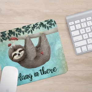 May include: A blue and green watercolor background with a sloth hanging upside down from a branch. The sloth is brown and has a cute face. There are red mushrooms on the branch and the text "Hang in there" is written in white on the bottom of the image.
