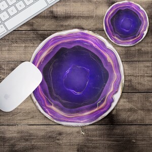 May include: Purple agate coaster with a white border and a swirling pattern. The coaster is on a wooden surface.