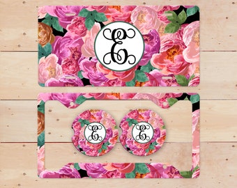May include: A pink and green floral design license plate frame with two matching coasters. The frame and coasters feature a black monogram with the letter "E".