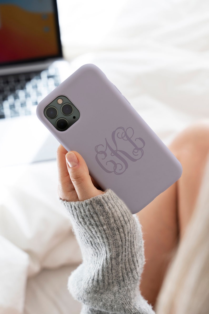 May include: A lavender phone case with a monogrammed design. The monogram is in a script font and is the letters "KH".