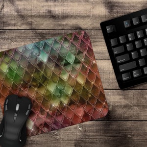May include: A mouse pad with a colorful, iridescent, glitter-like, scale pattern. The scales are in shades of green, blue, pink, and gold. The mouse pad is on a wooden surface.