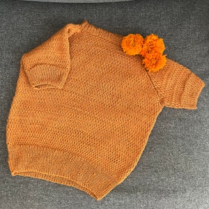 May include: A brown knitted sweater with a loose fit and short sleeves. The sweater is made with a textured stitch and has a relaxed, casual look.