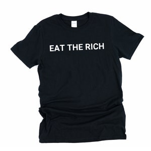 May include: Black t-shirt with the white text "EAT THE RICH". The shirt is a crew neck style and appears to be made of a soft material. The text is centered on the front of the shirt.