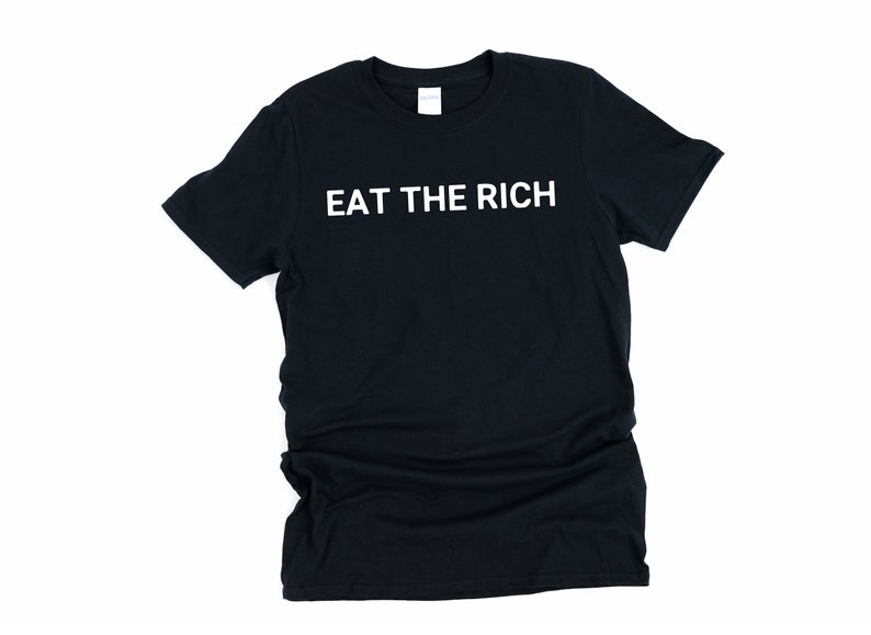 May include: Black t-shirt with the white text "EAT THE RICH". The shirt is a crew neck style and appears to be made of a soft material. The text is centered on the front of the shirt.