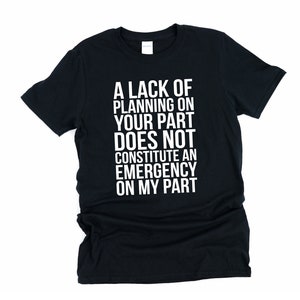 May include: Black t-shirt with the white text: "A LACK OF PLANNING ON YOUR PART DOES NOT CONSTITUTE AN EMERGENCY ON MY PART." The shirt is a crew neck style.