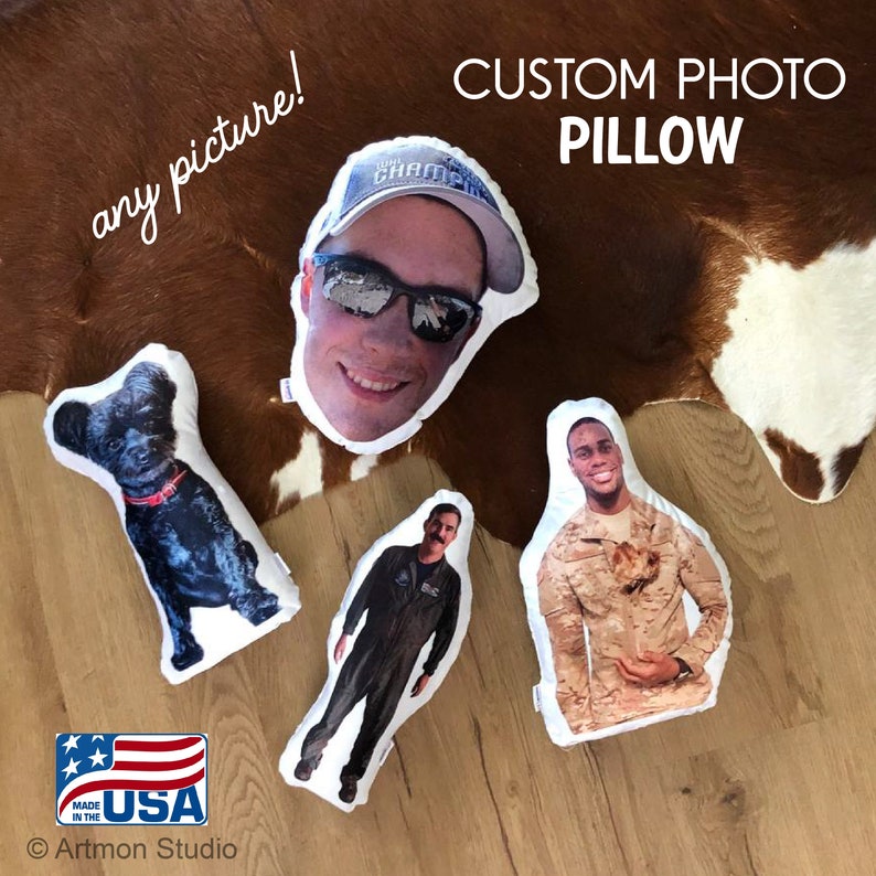 Pu&ograve; includere: Quattro cuscini personalizzati con foto su un tappeto di pelle di mucca marrone e bianco. I cuscini mostrano il viso di un uomo, un uomo in uniforme militare, un uomo in uniforme da pilota e un cane nero. I cuscini sono bianchi con un bordo bianco. Il testo "CUSTOM PHOTO PILLOW" &egrave; scritto in nero nella parte superiore dell'immagine.