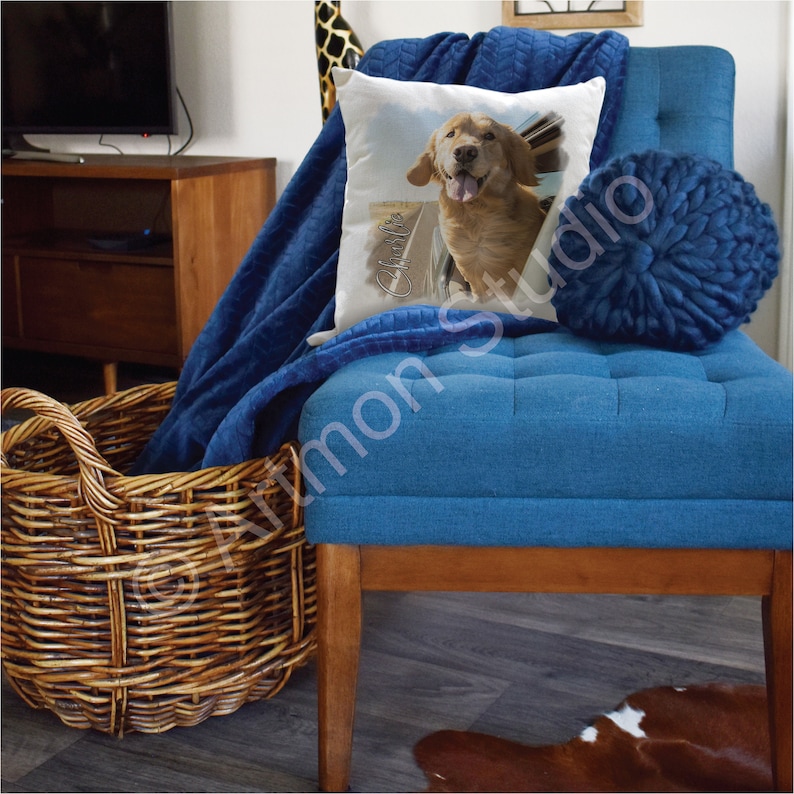 May include: A blue tufted ottoman with a brown wooden base. A white pillow with a golden retriever dog peeking out of a car window is on the ottoman. The pillow has the name "Charlie" written on it. A blue throw blanket is draped over the ottoman.