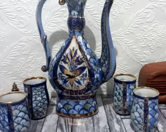 May include: A blue and gold ceramic teapot and six matching cups with intricate floral designs. The teapot has a tall, slender body and a curved spout. The cups are short and round with a scalloped rim.
